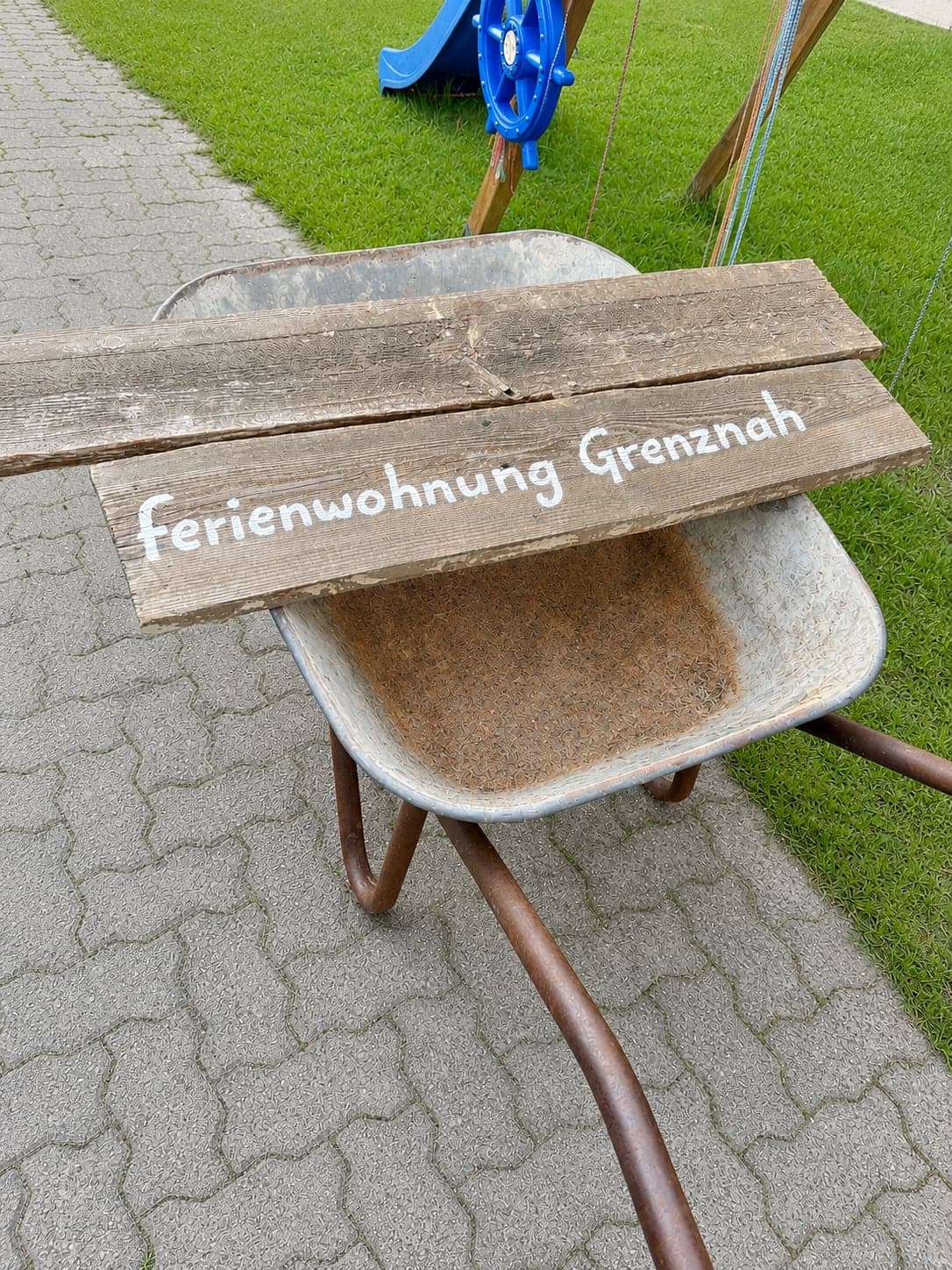 Handgemaltes Schild „Ferienwohnung Grenznah“ auf einer alten Schubkarre